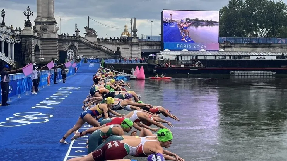 A triathlon swimmer diving into the Seine River under the Alexander III Bridge.