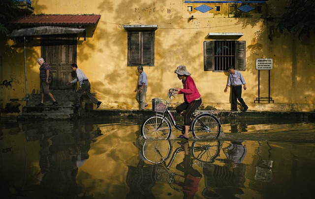 People on bicycles navigate through a flooded street in an urban area after heavy rainfall.